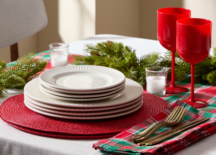 Holiday entertaining table setting featuring dinner plates, red drinkware and festive plaid table linens